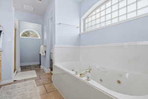 Bathroom featuring healthy amount of natural light, a whirlpool tub, stone tile flooring, and vanity