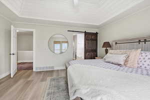 Bedroom with a barn door, wood finished floors, ensuite bathroom, ceiling fan, and crown molding