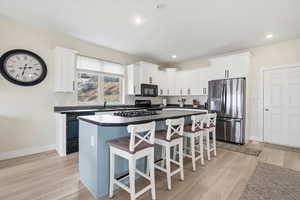 Kitchen featuring a kitchen island, a kitchen breakfast bar, black appliances, dark countertops, and white cabinets