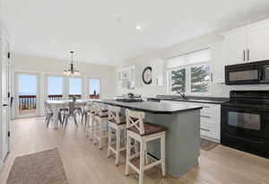 Kitchen with black appliances, a kitchen bar, dark countertops, a kitchen island, and white cabinetry