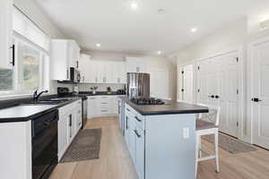 Kitchen featuring black appliances, dark countertops, white cabinets, a kitchen bar, and a center island
