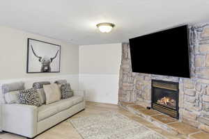 Living room with a wainscoted wall, wood finished floors, and a stone fireplace