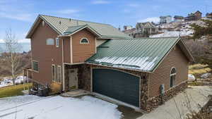 Rustic home with a metal roof, a garage, stone siding, and a standing seam roof