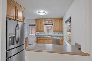 Kitchen with stainless steel appliances, dark countertops, brown cabinets, and a textured ceiling