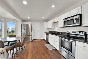 Kitchen with stainless steel appliances, white cabinets, dark countertops, dark wood finished floors, and recessed lighting