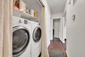 Laundry area featuring dark wood-type flooring, washer and dryer, a textured wall, and a textured ceiling