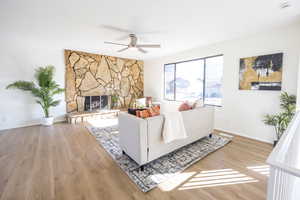 Living area featuring light wood finished floors, ceiling fan, and a fireplace