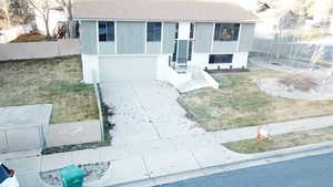 Raised ranch with concrete driveway, roof with shingles, and a garage