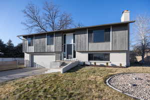View of front facade featuring driveway, brick siding, a garage, and a chimney