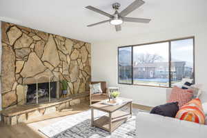 Living room featuring wood finished floors, a stone fireplace, and a ceiling fan
