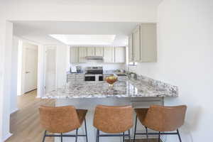 Kitchen with stainless steel electric range oven, a breakfast bar area, a peninsula, light stone countertops, and light wood finished floors