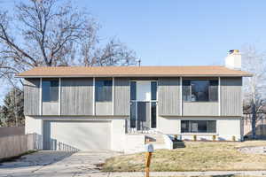 Bi-level home featuring brick siding, driveway, a chimney, and a garage