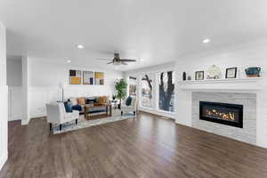 Living area with recessed lighting, dark wood-type flooring, a wainscoted wall, a stone fireplace, and ceiling fan