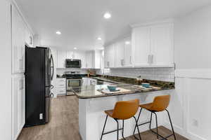 Kitchen with dark stone countertops, a peninsula, a kitchen bar, stainless steel appliances, and white cabinetry