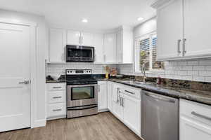 Kitchen featuring appliances with stainless steel finishes, dark stone countertops, white cabinets, light wood-style flooring, and recessed lighting