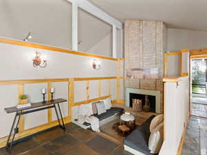 Living area featuring lofted ceiling, a brick fireplace, stone tile floors, and a baseboard heating unit
