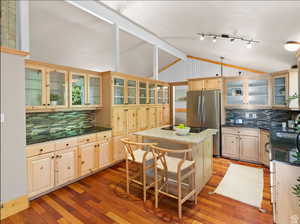 Kitchen with light brown cabinets, tasteful backsplash, glass insert cabinets, a breakfast bar area, and dark stone countertops