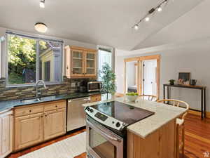 Kitchen featuring dark stone countertops, stainless steel appliances, lofted ceiling, light brown cabinetry, and light wood-style floors