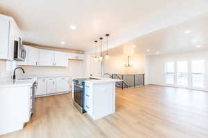 Kitchen featuring a kitchen island, white cabinets, appliances with stainless steel finishes, light wood finished floors, and recessed lighting