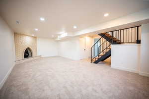 Unfurnished living room with light colored carpet, recessed lighting, a brick fireplace, and stairway