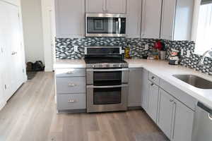 Kitchen featuring gray cabinets, stainless steel appliances, light stone counters, light wood laminate  flooring, and decorative backsplash