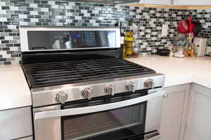 Kitchen view of stainless steel gas range oven, light stone counters, and decorative backsplash