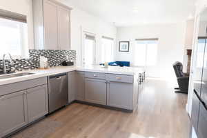 Kitchen with gray cabinets, open floor plan, a peninsula, stainless steel dishwasher, and light wood laminate floors