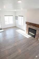 Unfurnished living room featuring a stone fireplace, a textured ceiling, and dark wood-style flooring