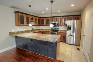 Kitchen with glass insert cabinets, appliances with stainless steel finishes, a peninsula, decorative light fixtures, and a breakfast bar area