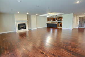 Unfurnished living room with a tiled fireplace, dark wood-style floors, a chandelier, and recessed lighting