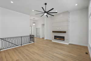 Unfurnished living room featuring a glass covered fireplace, a ceiling fan, light wood-style flooring, and recessed lighting