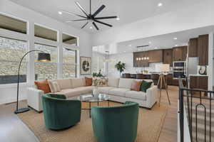 Enhanced staged photo Living area featuring a ceiling fan, light wood-style flooring, a high ceiling, and recessed lighting