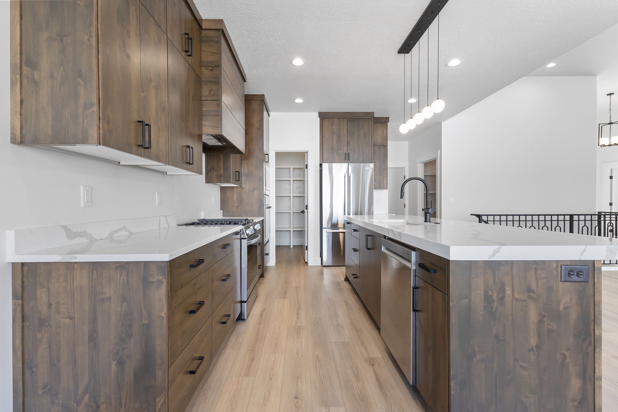 Kitchen with modern cabinets, light wood-style flooring, decorative light fixtures, stainless steel appliances, and a kitchen island with sink