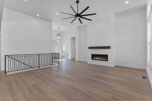 Unfurnished living room with a large fireplace, a ceiling fan, wood finished floors, a high ceiling, and recessed lighting