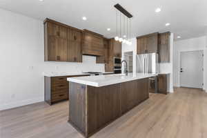 Kitchen with stainless steel appliances, pendant lighting, light stone counters, and light wood-type flooring