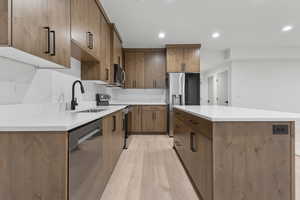 Kitchen with appliances with stainless steel finishes, light wood-style floors, brown cabinetry, a center island, and recessed lighting
