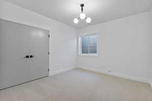 Unfurnished bedroom featuring a closet, light colored carpet, and a chandelier