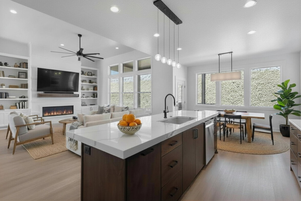 Enhanced staged photo Kitchen featuring dark wood finish cabinetry, decorative light fixtures, an island with sink, a fireplace, and light stone countertops