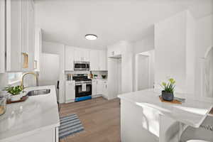 Kitchen featuring appliances with stainless steel finishes, white cabinets, light wood finished floors, a breakfast bar, and light stone countertops