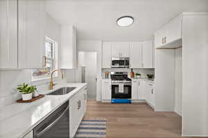 Kitchen featuring appliances with stainless steel finishes, white cabinetry, light wood-type flooring, and light stone counters