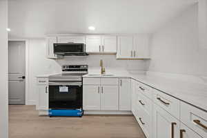 Kitchen featuring stainless steel electric range, white cabinetry, light wood-style flooring, light stone countertops, and black microwave