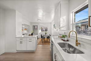 Kitchen with white cabinets, light wood-style flooring, a peninsula, and light stone counters