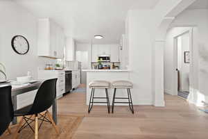 Kitchen with white cabinetry, a breakfast bar, light countertops, light wood-style floors, and arched walkways
