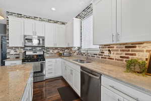 Kitchen with stainless steel appliances, white cabinets, light stone countertops, and recessed lighting