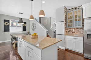 Kitchen with white cabinets, decorative light fixtures, light stone countertops, stainless steel fridge with ice dispenser.