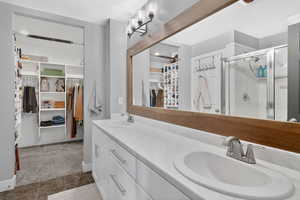 Bathroom featuring a walk in closet, a stall shower, double vanity, and dark colored carpet