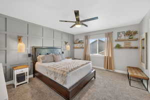 Carpeted bedroom featuring ceiling fan and a decorative wall