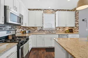Kitchen with stainless steel appliances, white cabinetry, light stone countertops, brick wall, and laminate floors