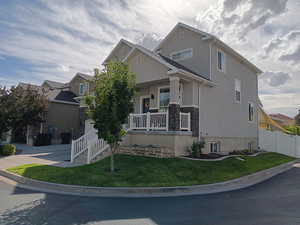 View of front of house featuring covered porch, stucco siding, a front yard, and stone siding