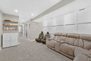 Living area featuring light colored carpet, a decorative wall, and recessed lighting